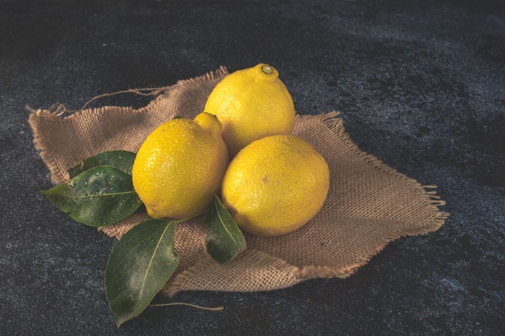 Three ripe lemons placed on burlap, accompanied by green leaves, highlighting freshness and rustic charm.